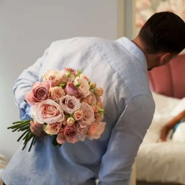 En man som håller en stor bukett av rosa rosor bakom ryggen