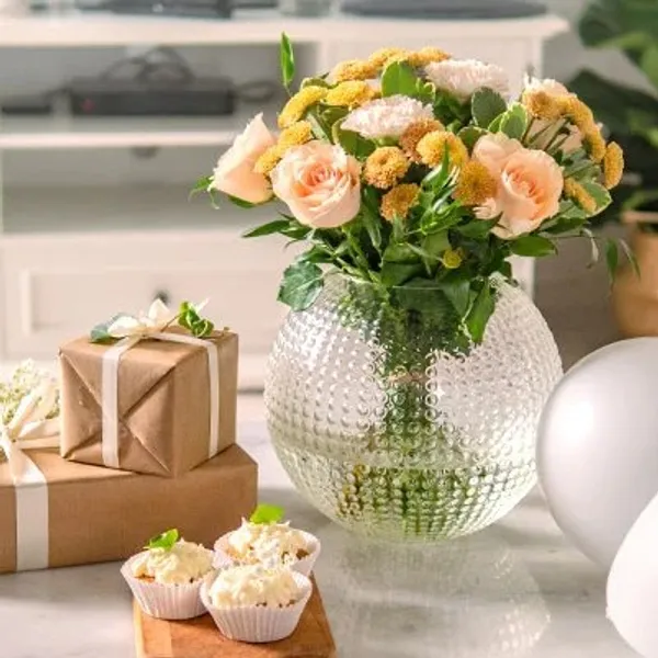 A bunch of flowers in a vase, next to presents and cupcakes