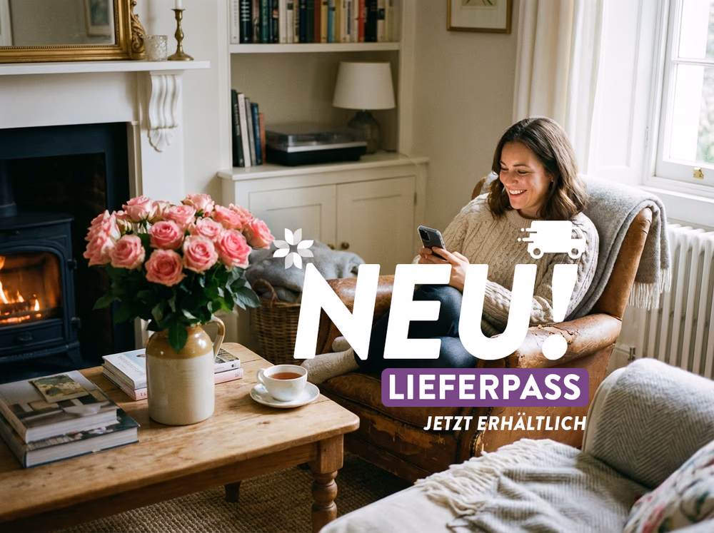 frau die in ihrem wohnzimmer sitzt und blumen online ueber ihr handy bestellet, neben ihr ein blumenstrauss