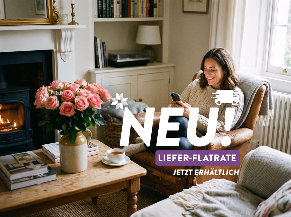 frau die in ihrem wohnzimmer sitzt und blumen online ueber ihr handy bestellet, neben ihr ein blumenstrauss