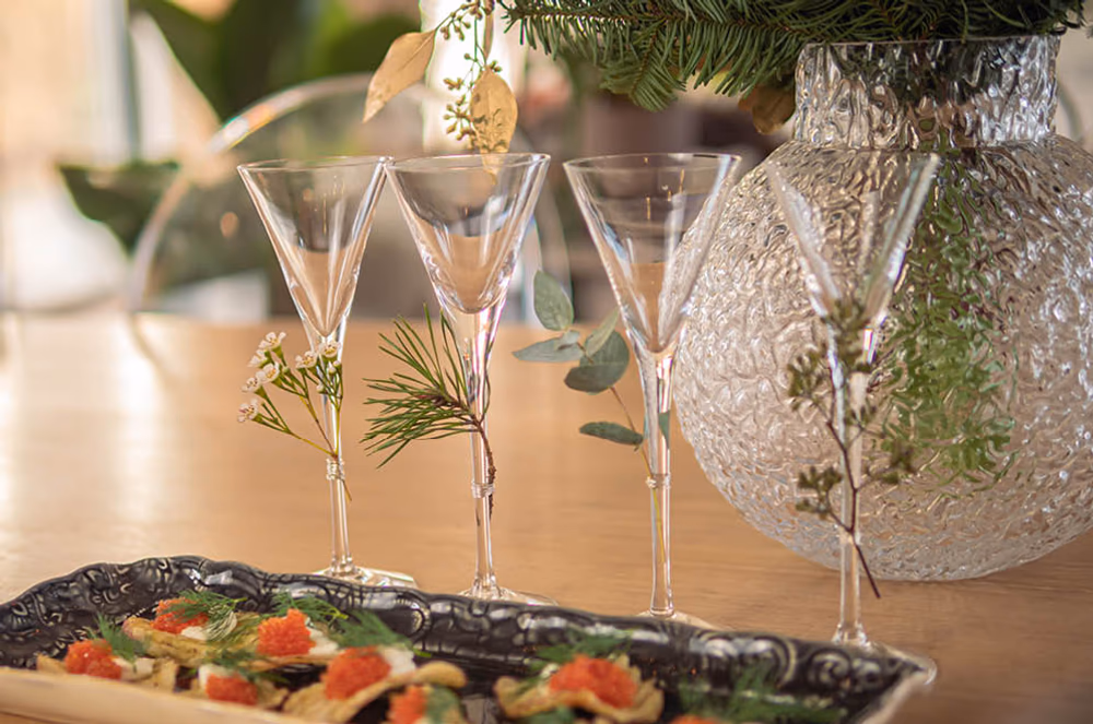 Vinglass dekorert med grønne elementer på et bord med en vase og mat.