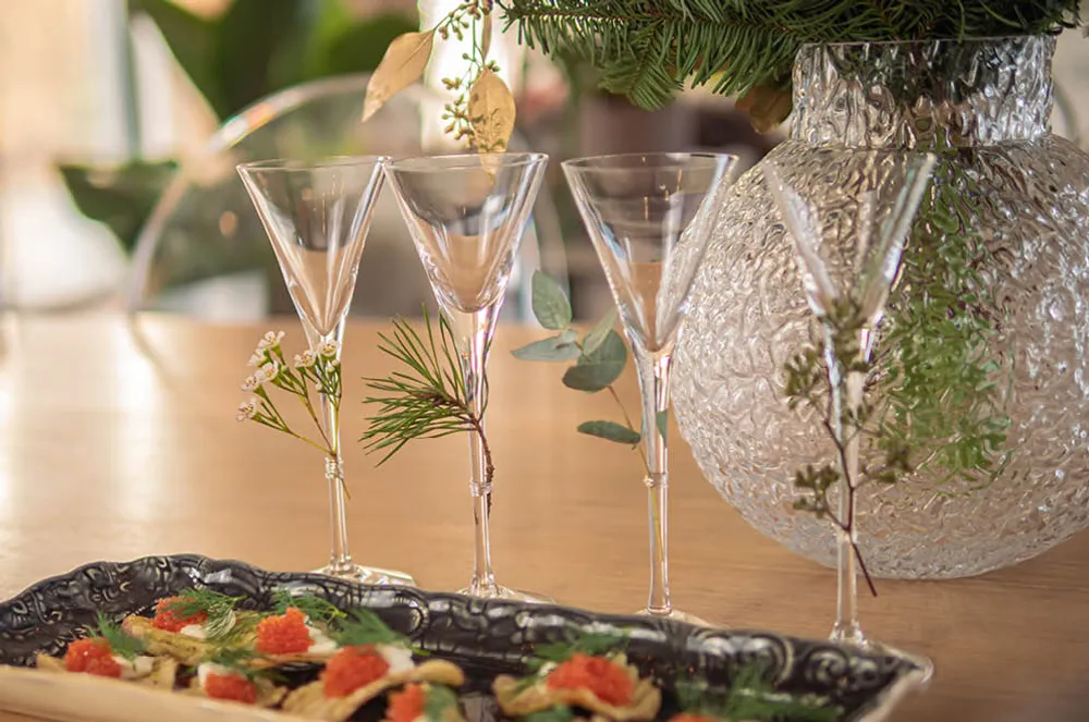 wine glasses decorated with greenery on a table with a vase and food