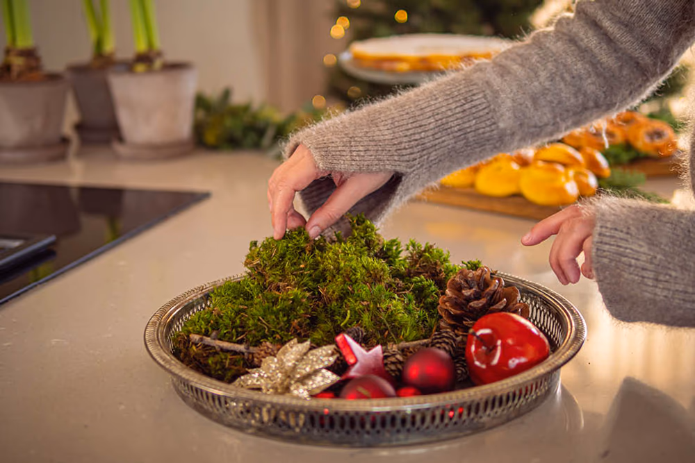 En bolle med kongler, epler, juledekorasjoner og grønt.