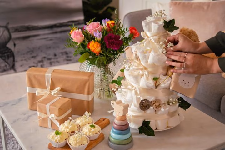 en färgglad bukett av rosa rosor, orangea rosor och vinröda nejlikor tillsammans med presenter till babyshower.